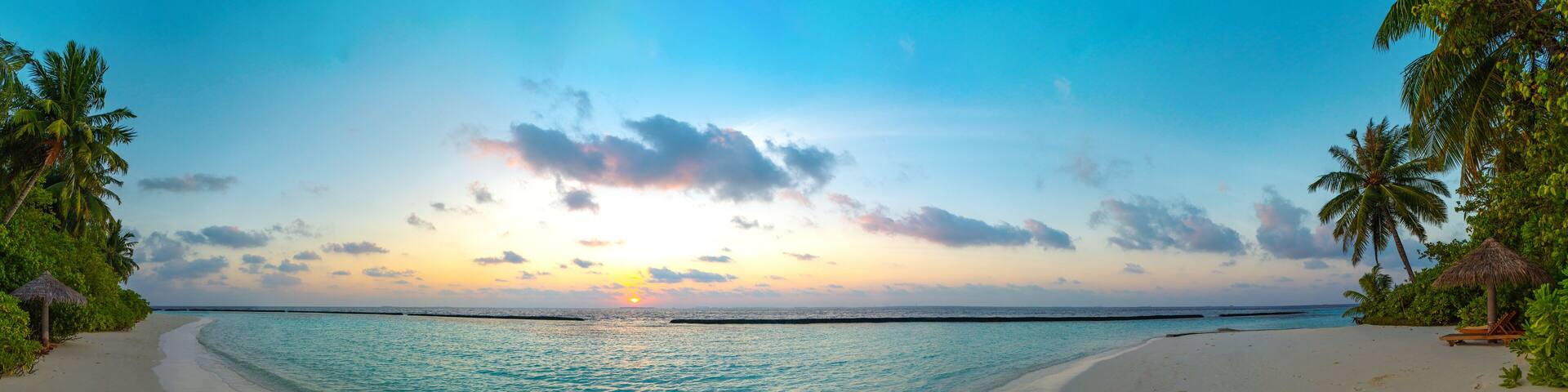 Amazing wide panorama of tropical Maldives island. Exotic beach background with blue lagoon, turquoise water and palm trees during beautiful sunrise.