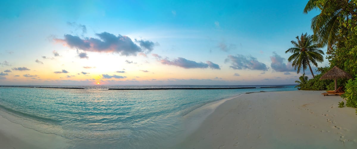 A beach with clear turquoise water, palm trees, and a thatched hut.
