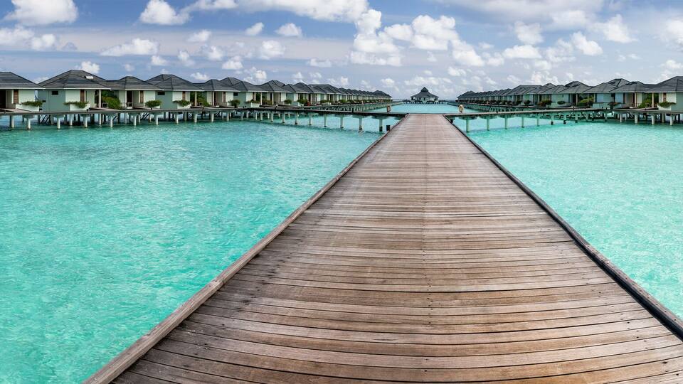 A wooden pier leading to overwater bungalows in clear turquoise waters.