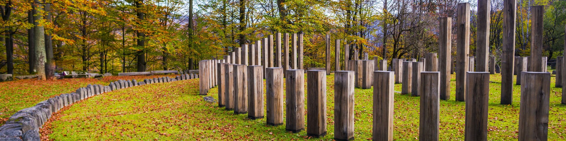 Un parque con un sendero circular de piedra, postes de madera y árboles otoñales.