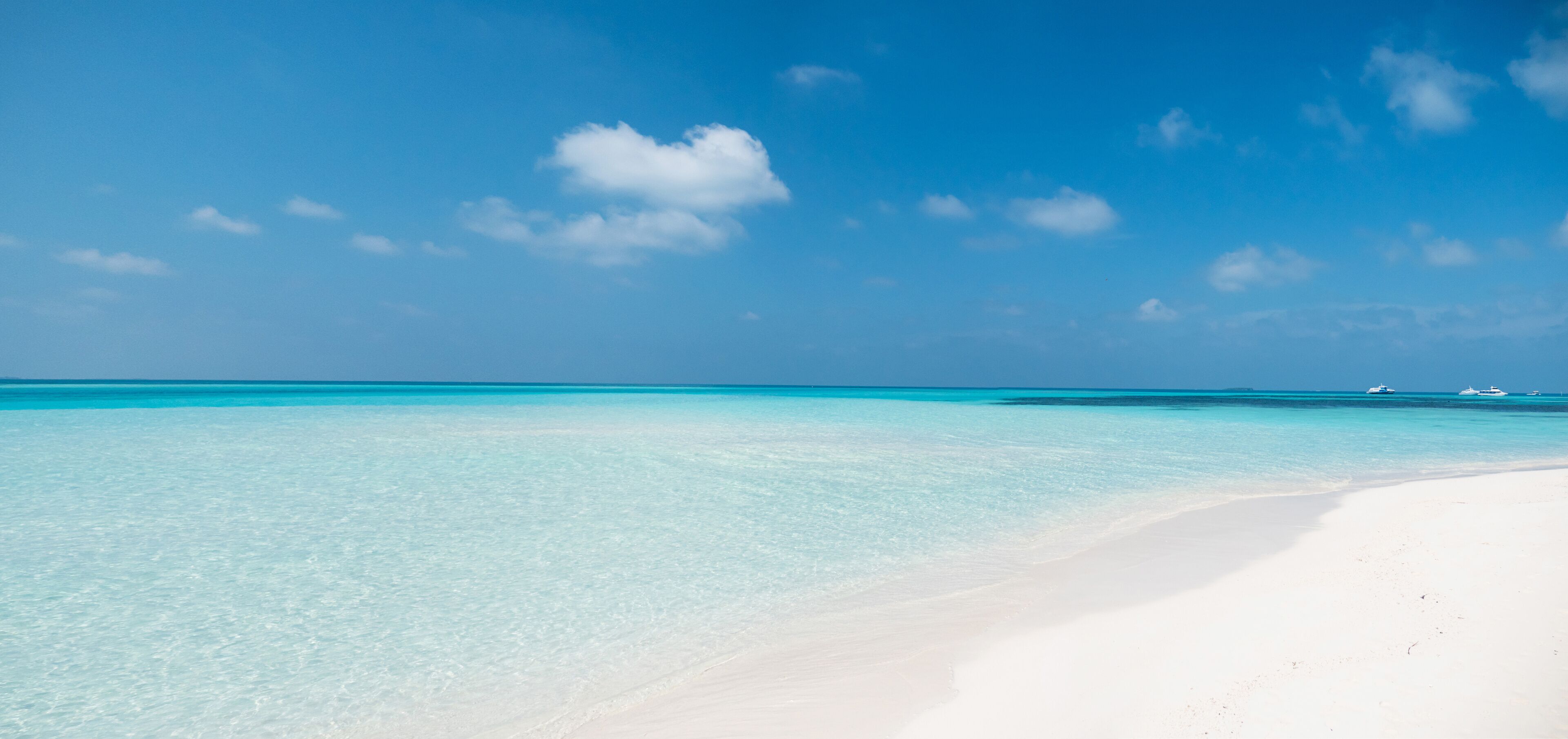 A beach with clear turquoise water and a white sandy shore under a blue sky with scattered clouds.