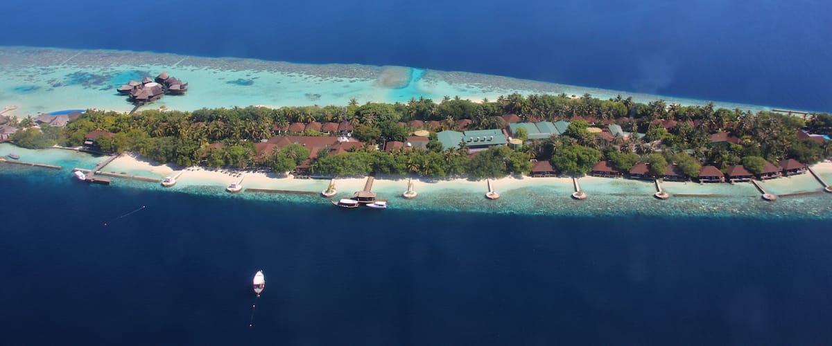 An aerial view of a tropical island with clear turquoise waters, a sandy beach, and overwater bungalows.