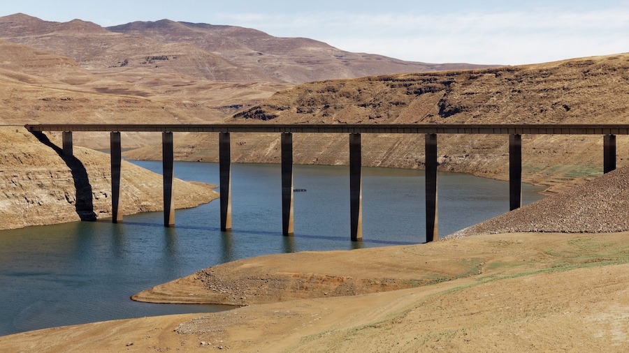A bridge over a calm river with a dry, hilly landscape in the background.