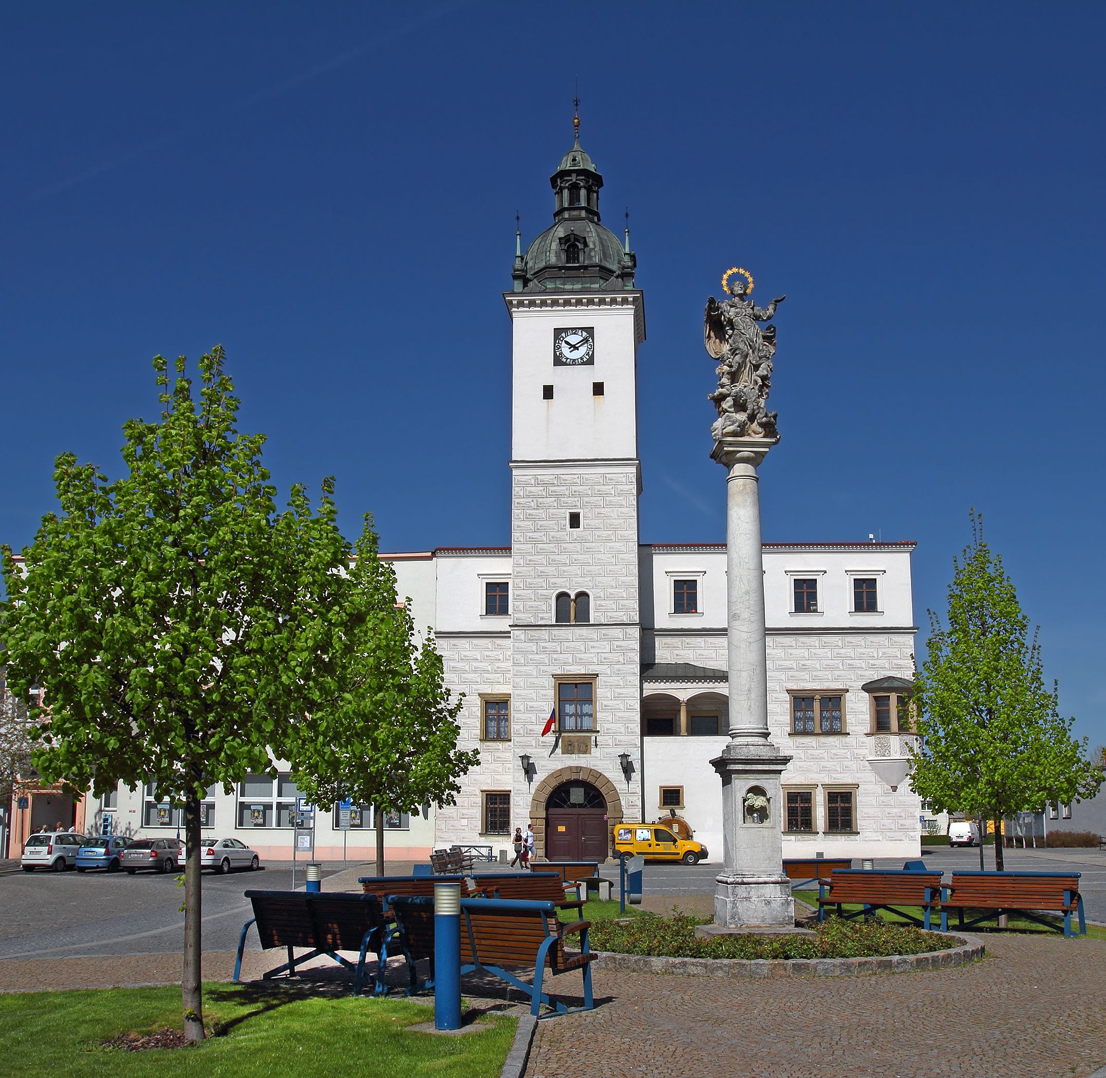 Ein historisches Gebäude mit einem Glockenturm, einer Statue und einem Park mit Bänken.