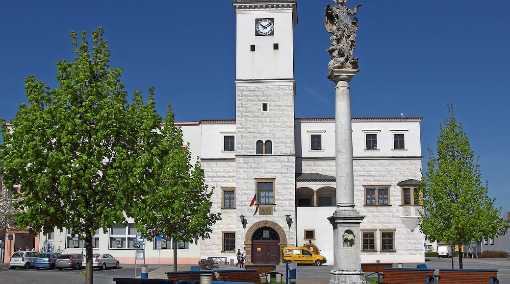Ein historisches Gebäude mit einem Glockenturm, einer Statue und einem Park mit Bänken.