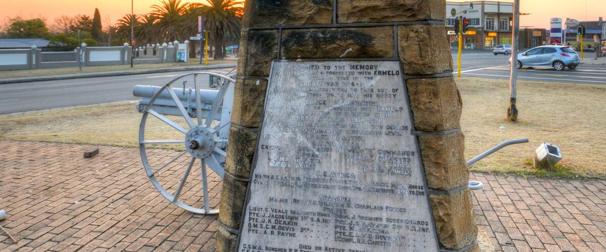 A stone monument with an inscription, located in a paved area with a sunset in the background.