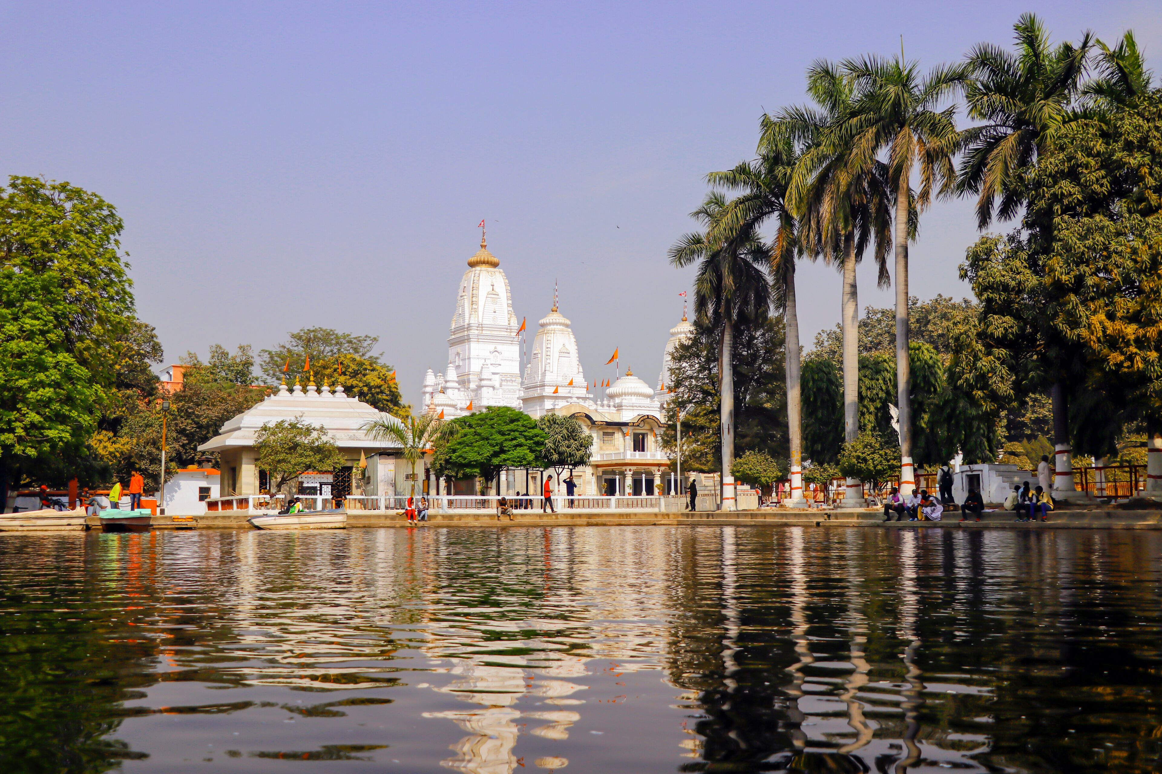 A white temple with multiple domes, palm trees, and a calm body of water.
