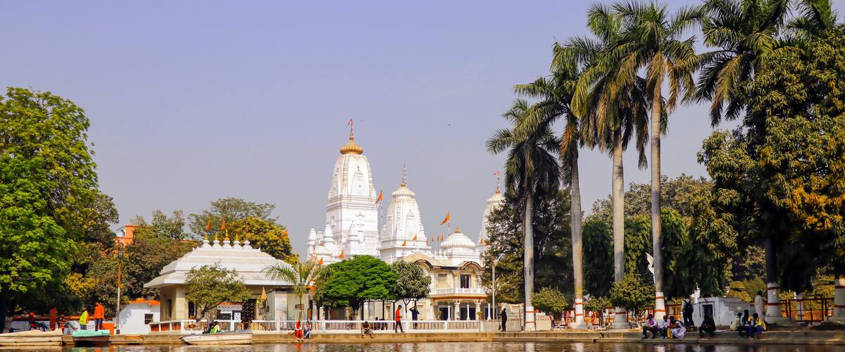 A white temple with multiple domes, palm trees, and a calm body of water.