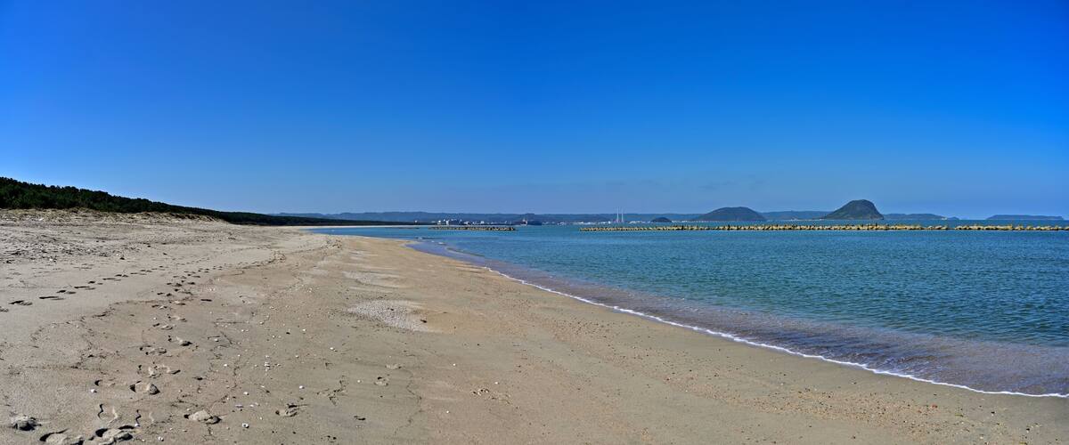 A sandy beach with gentle waves, a clear blue sky, and distant mountains.