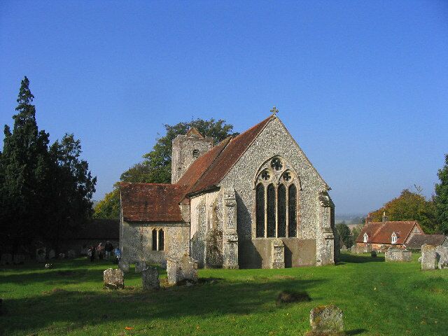 An old stone church with a red roof and a bell tower, surrounded by a grassy cemetery with gravestones.
