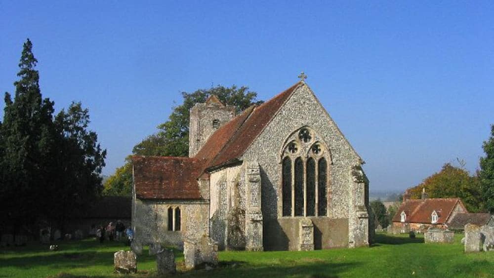An old stone church with a red roof and a bell tower, surrounded by a grassy cemetery with gravestones.