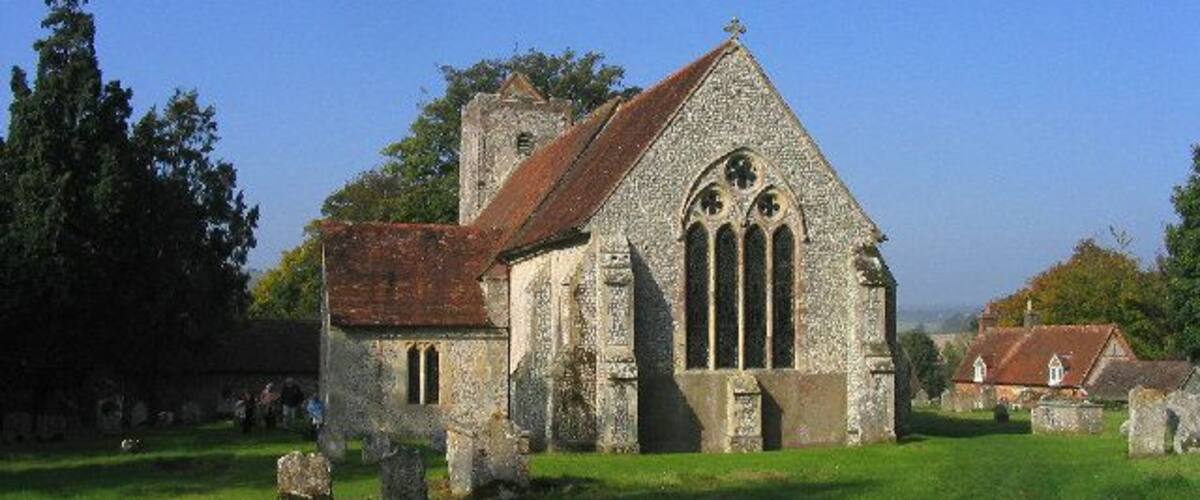 An old stone church with a red roof and a bell tower, surrounded by a grassy cemetery with gravestones.