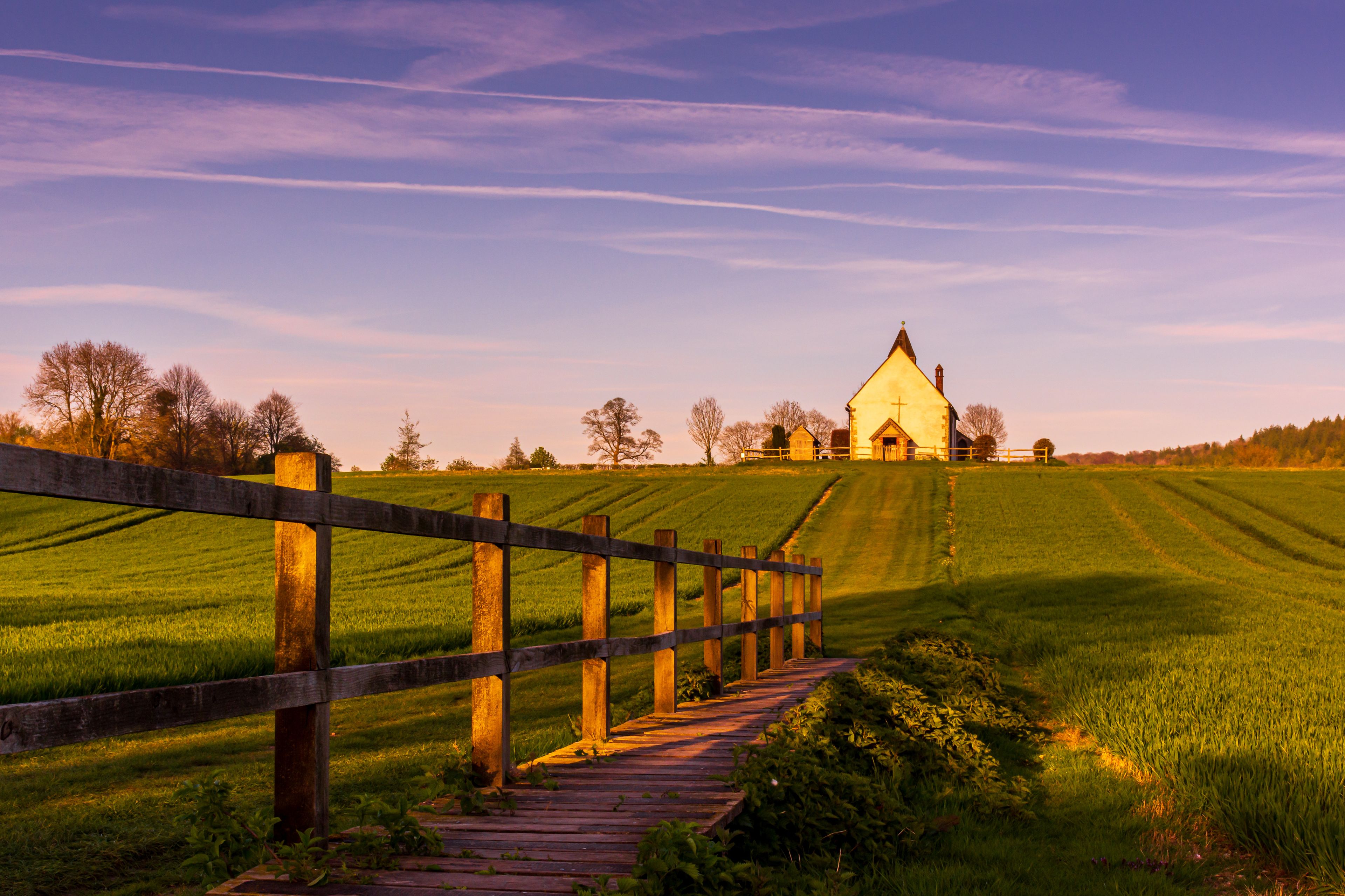 A wooden fence leading to a church on a hill with a clear sky.