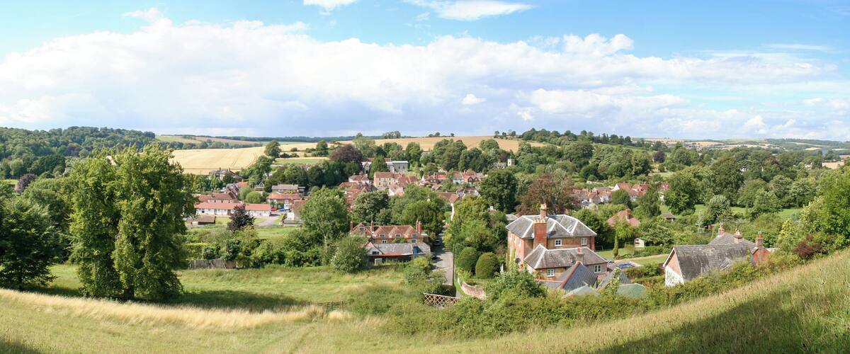 A rural village nestled in a valley with rolling hills and scattered trees.