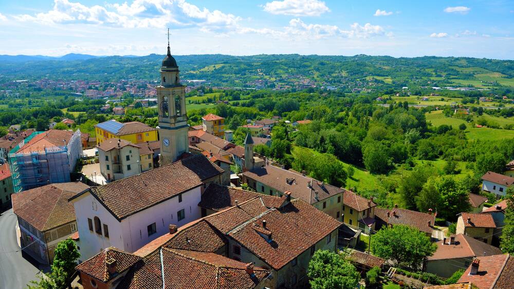 A town with a prominent church tower, surrounded by lush green hills and a clear blue sky.