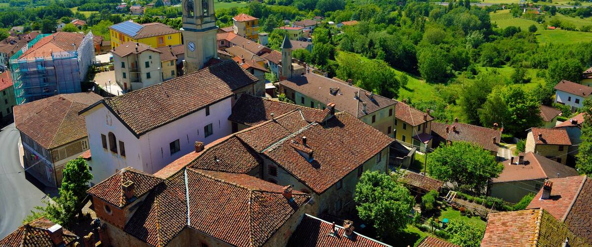 A town with a prominent church tower, surrounded by lush green hills and a clear blue sky.