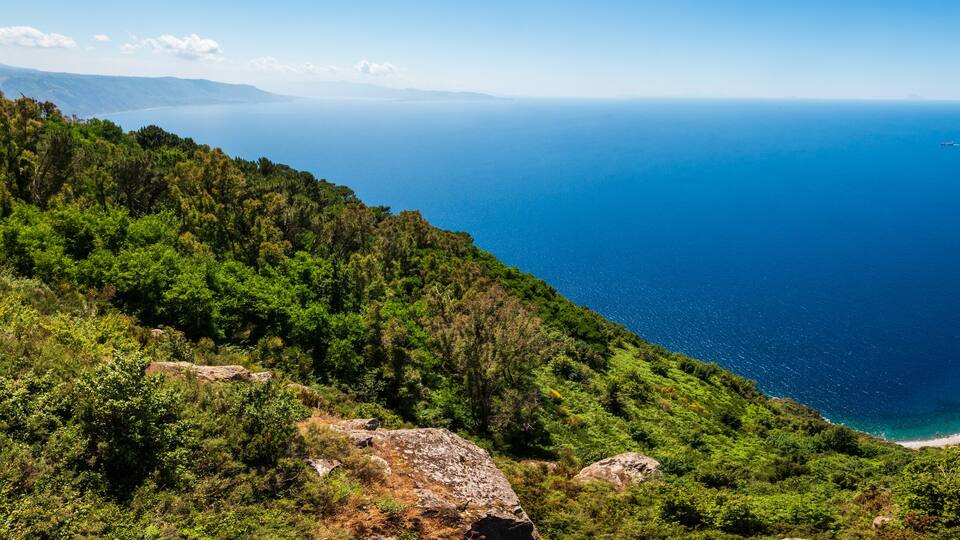 A coastal landscape with a deep blue sea, green hills, and rocky cliffs.