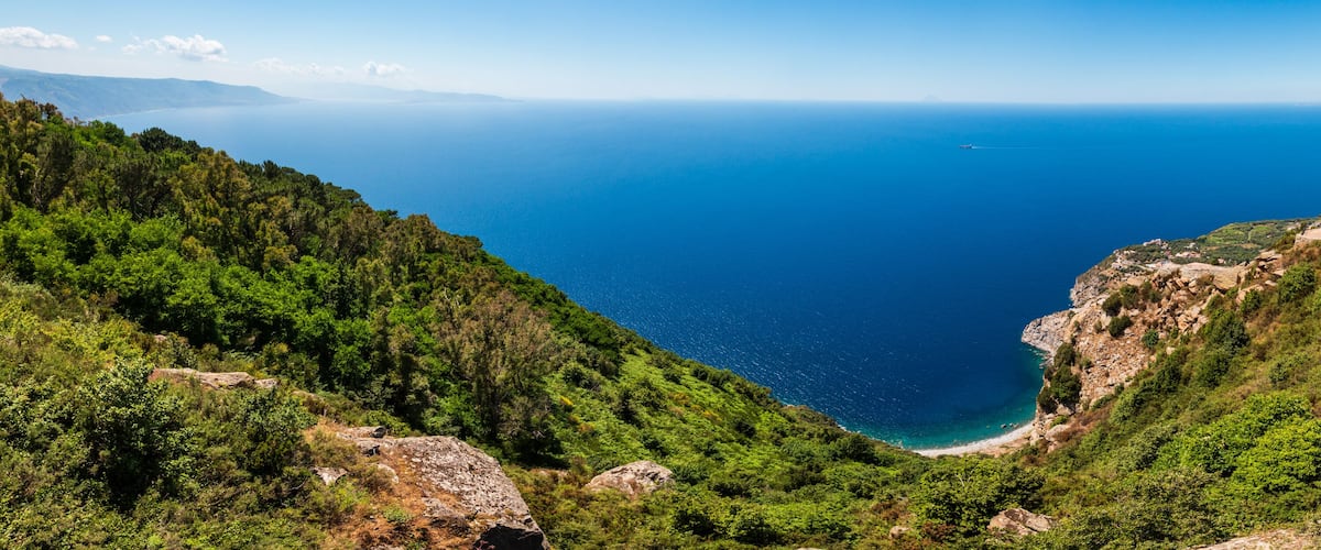 A coastal landscape with a deep blue sea, green hills, and rocky cliffs.