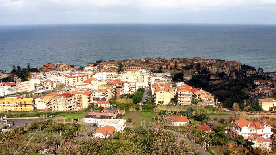A coastal town with buildings near the sea and a prominent cliff.