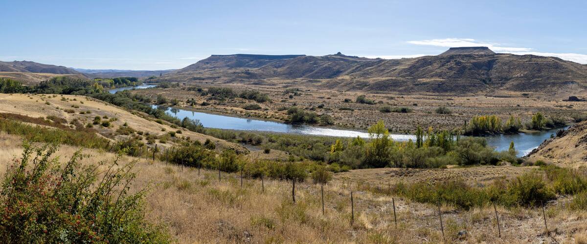 A river winding through a dry, hilly landscape with sparse vegetation and distant mountains.