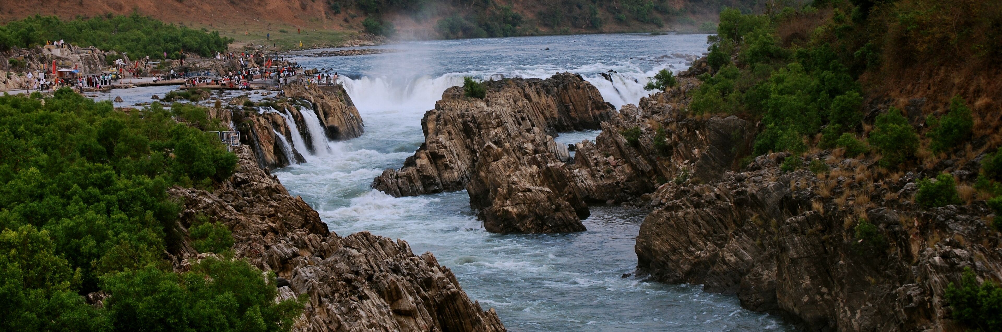 A waterfall cascading over rocky terrain with a river below, surrounded by dense greenery.