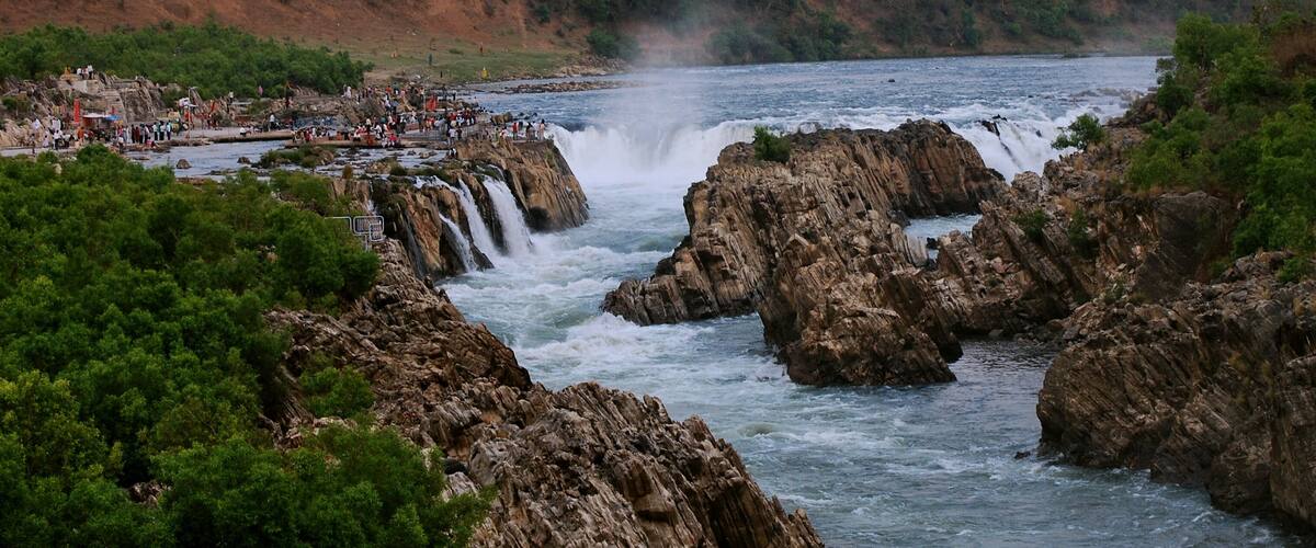 A waterfall cascading over rocky terrain with a river below, surrounded by dense greenery.