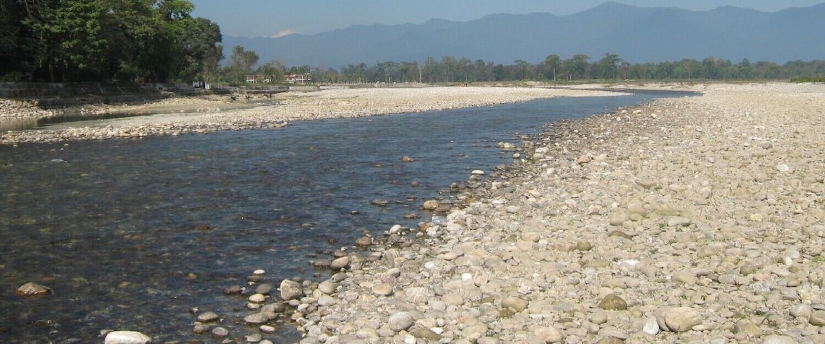 A river with a rocky bank, trees, and mountains in the background.