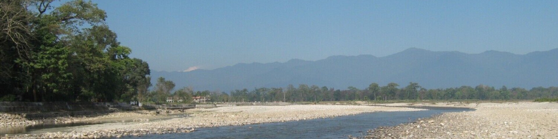 A river with a rocky bank, trees, and mountains in the background.