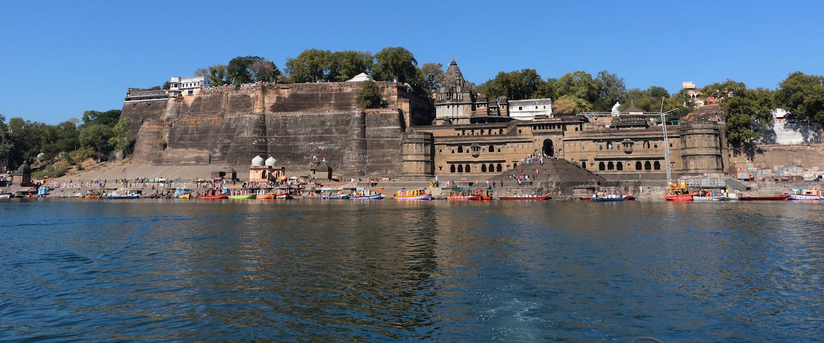 A riverside view with boats, a fort, and a temple.