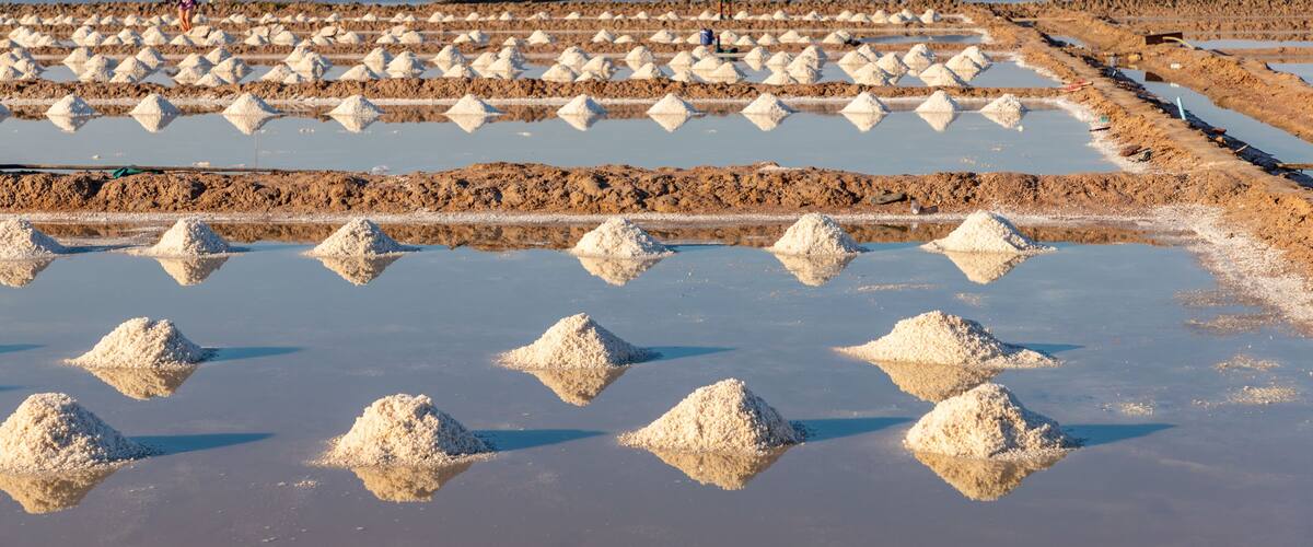 A salt flat with white salt formations and people working in the background.