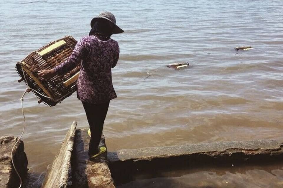A person carrying a large basket across a wooden bridge over a body of water.