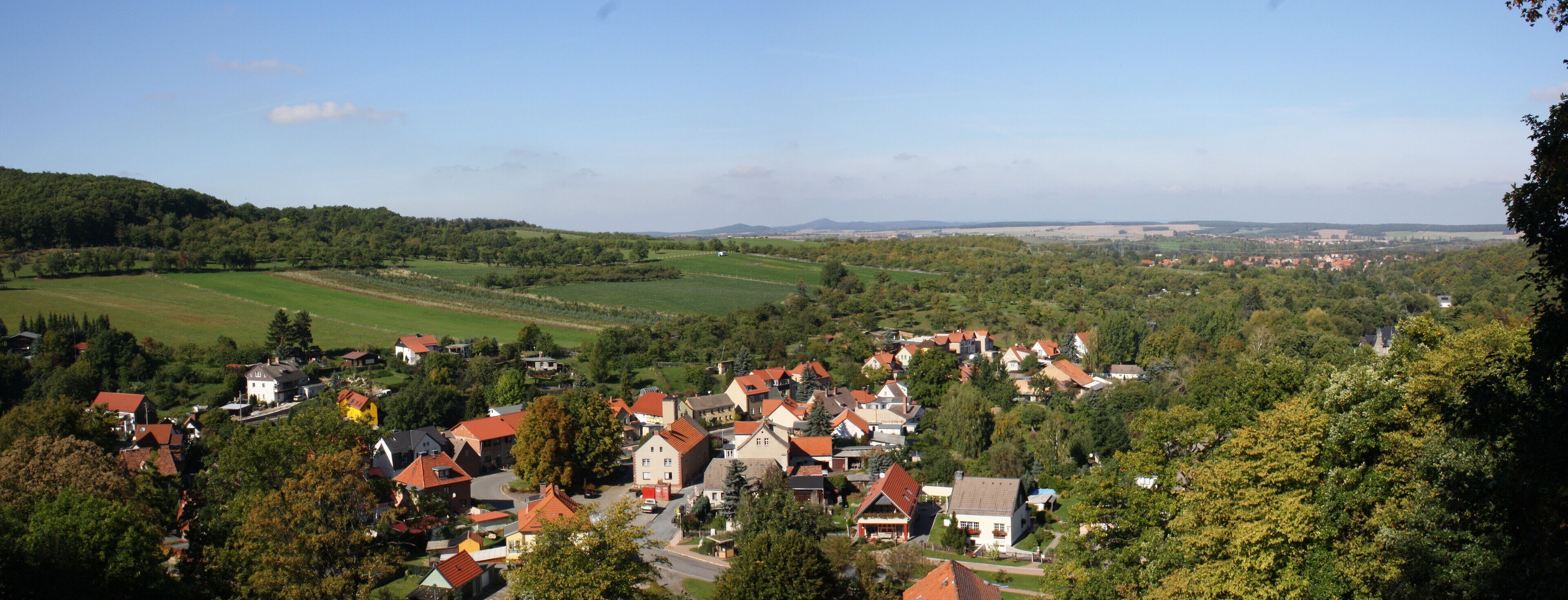 A village nestled in a valley with green fields and houses with red roofs.