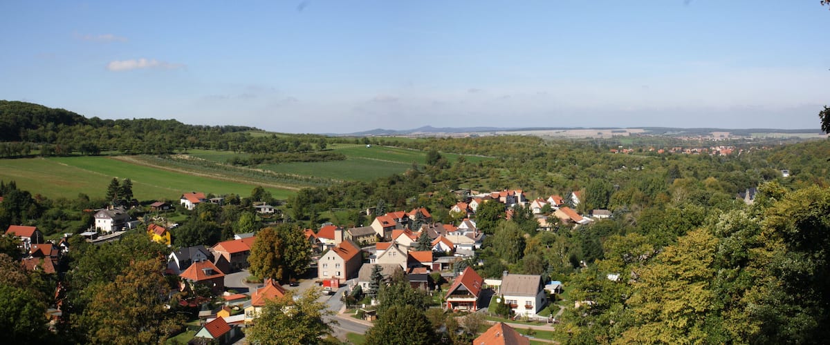 A village nestled in a valley with green fields and houses with red roofs.