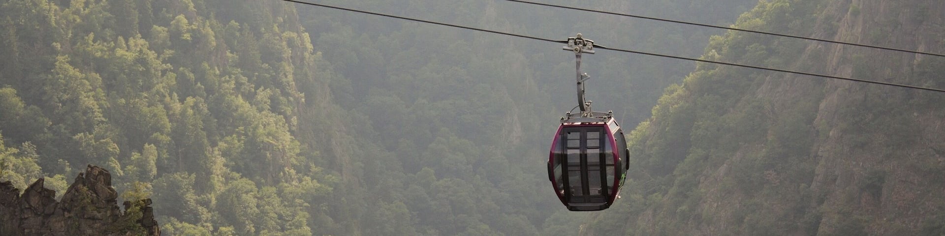 A cable car suspended over a forested valley with rocky cliffs.