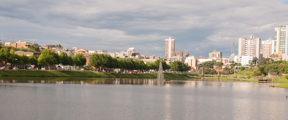 A lake with a fountain in the center, surrounded by trees and buildings in the background.