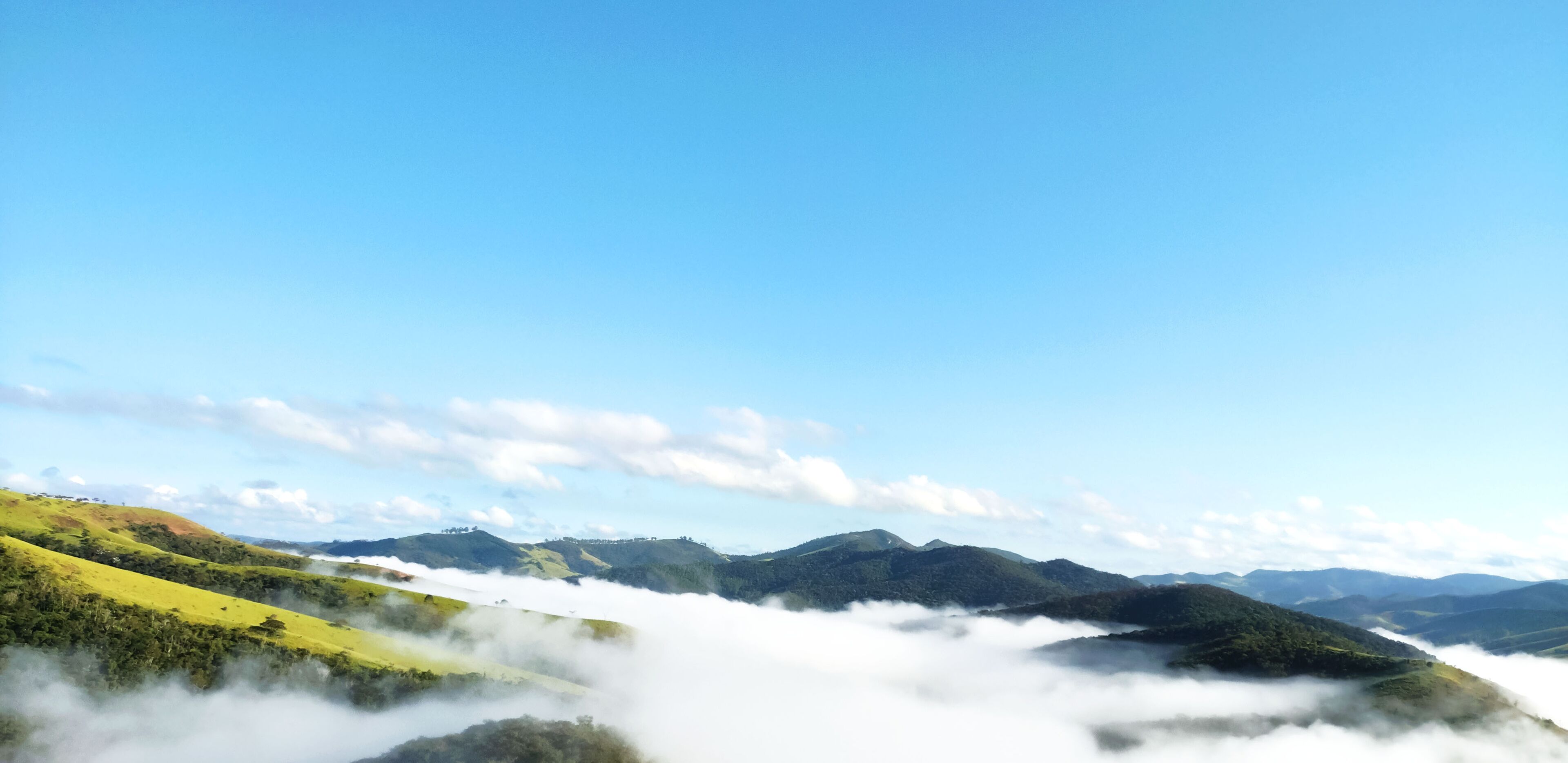 A landscape with rolling hills, a valley, and a mountain range under a clear blue sky.