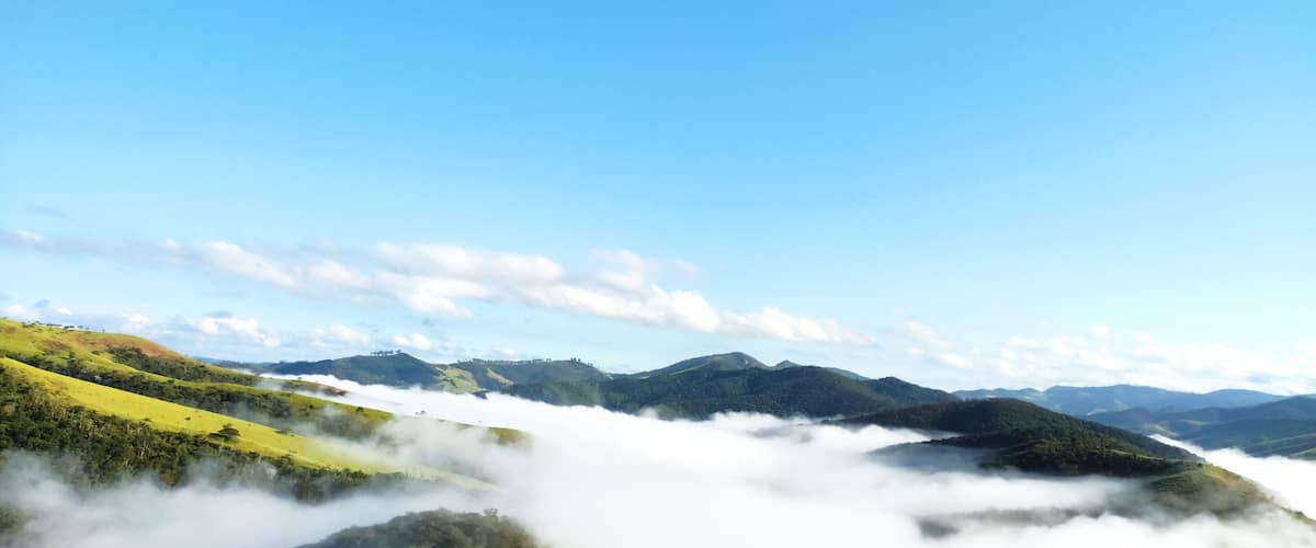 A landscape with rolling hills, a valley, and a mountain range under a clear blue sky.
