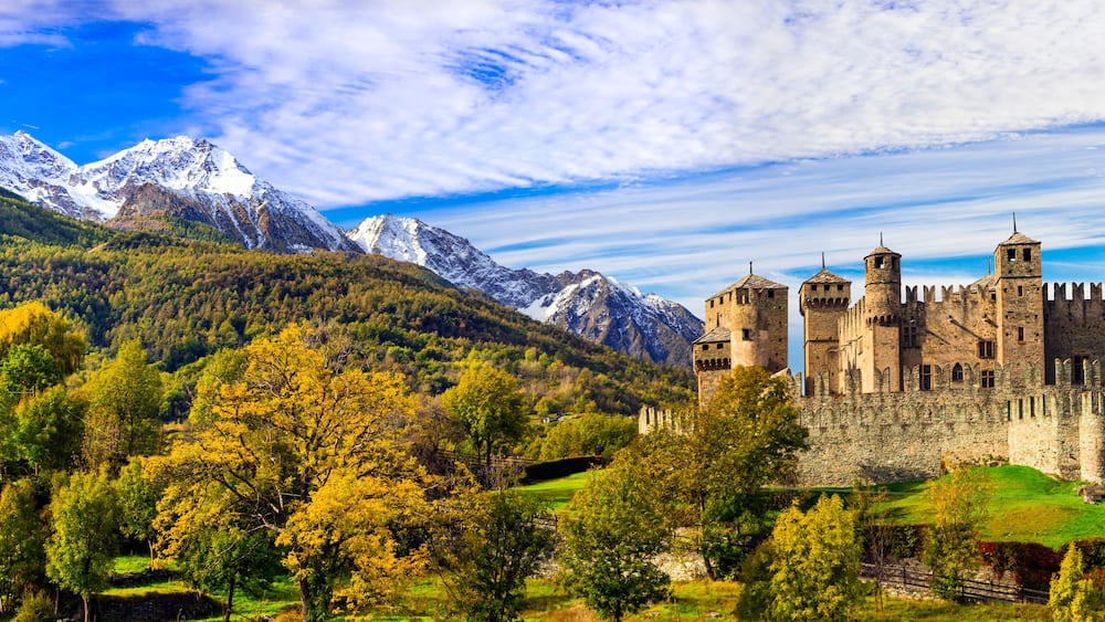 A castle surrounded by mountains and autumn foliage.