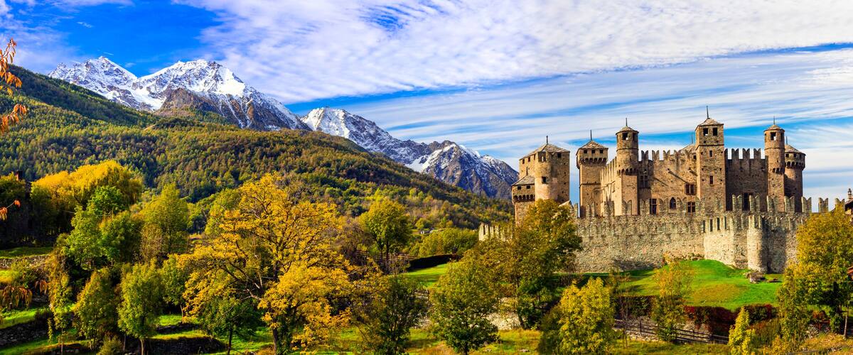 Eine Burg, umgeben von Bergen und Herbstlaub.