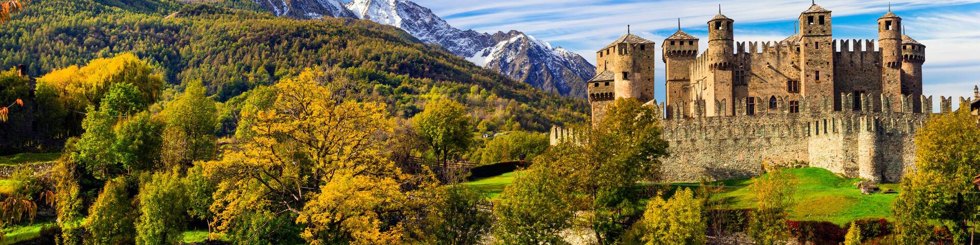 A castle surrounded by mountains and autumn foliage.