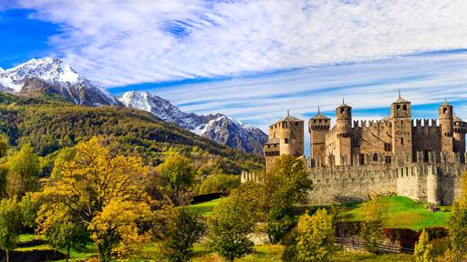 A castle surrounded by mountains and autumn foliage.