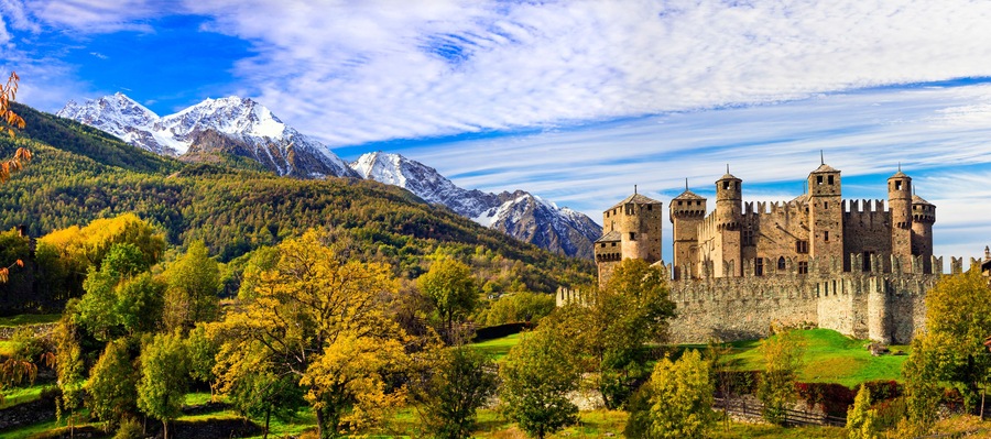 A castle surrounded by mountains and autumn foliage.