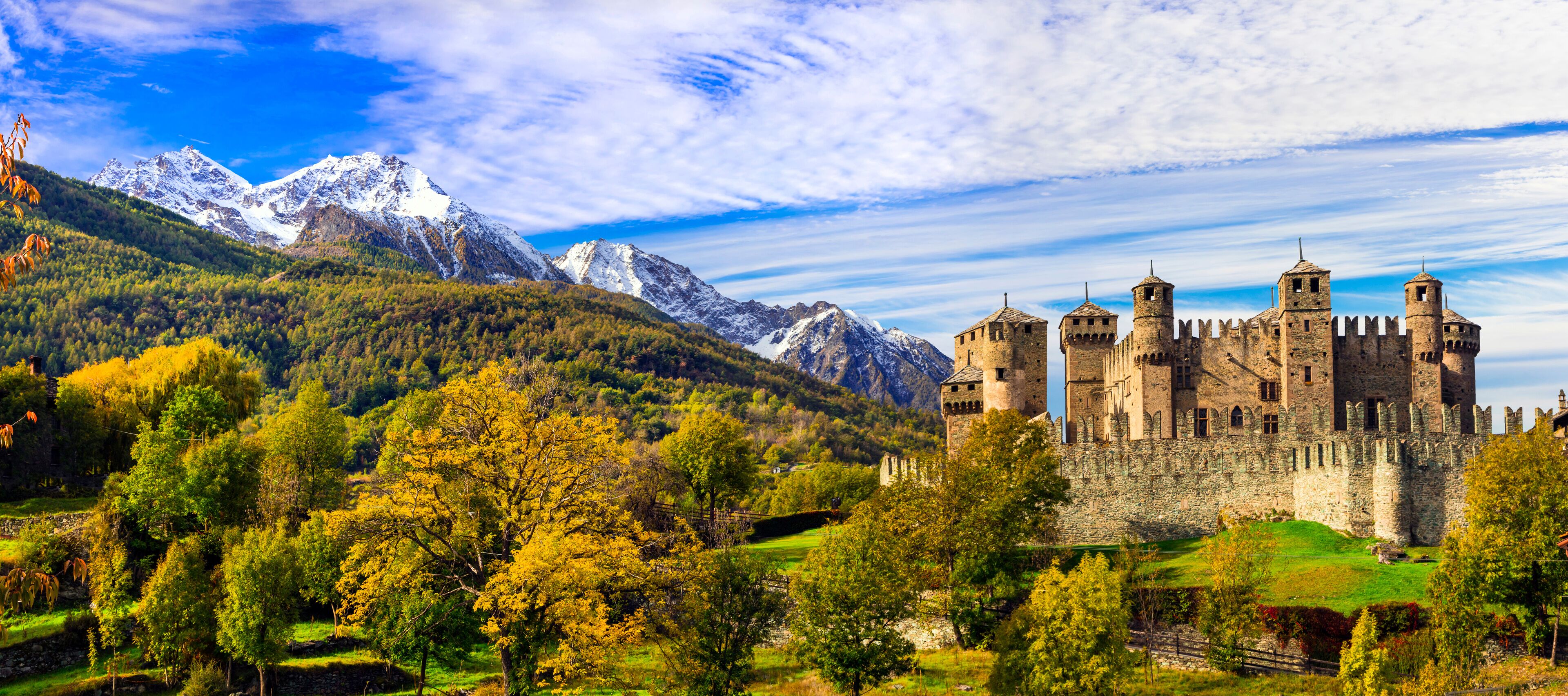 A castle surrounded by mountains and autumn foliage.
