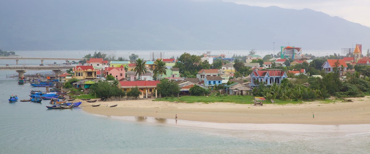 A coastal town with colorful houses, a beach, boats, and a bridge in the background.