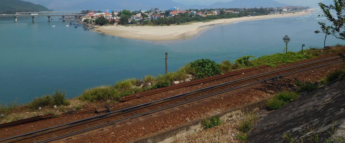 A coastal town with a beach, a bridge, and mountains in the background.