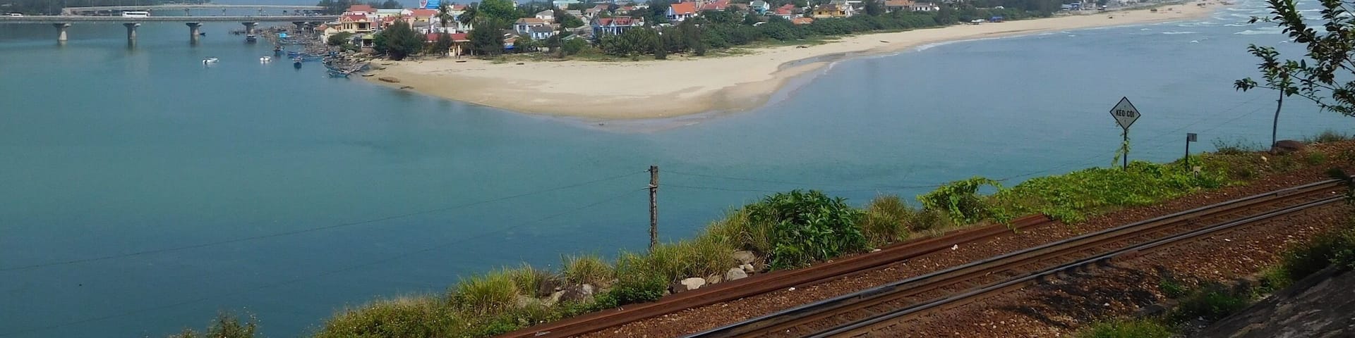 A coastal town with a beach, a bridge, and mountains in the background.
