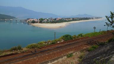 Un pueblo costero con playa, un puente y montañas al fondo.