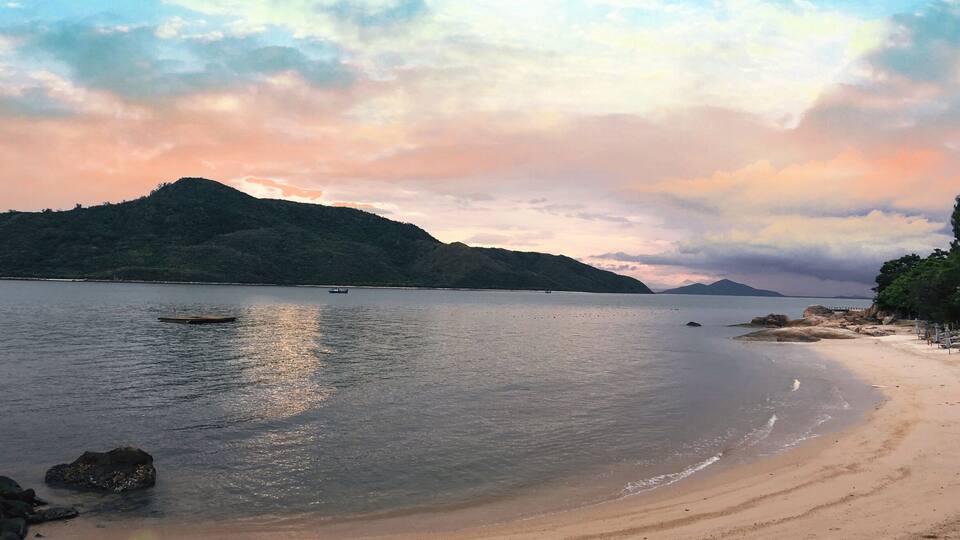 A calm beach with clear water, a boat, and a mountain in the background.