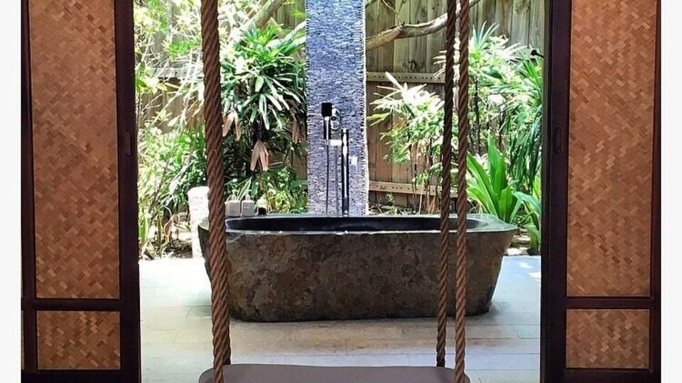 A swing chair in a covered area with a stone fountain and lush greenery in the background.