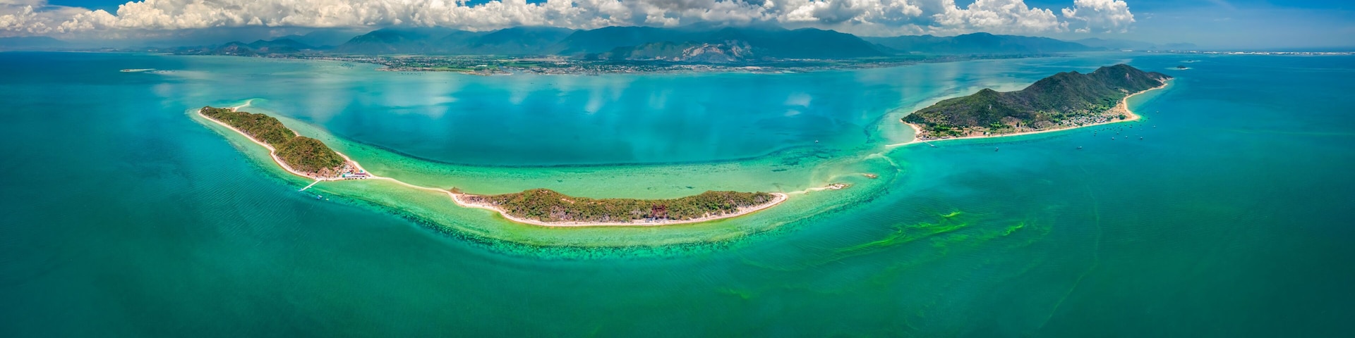 Una isla tropical con aguas turquesas cristalinas, una costa en forma de media luna y una cadena montañosa al fondo.